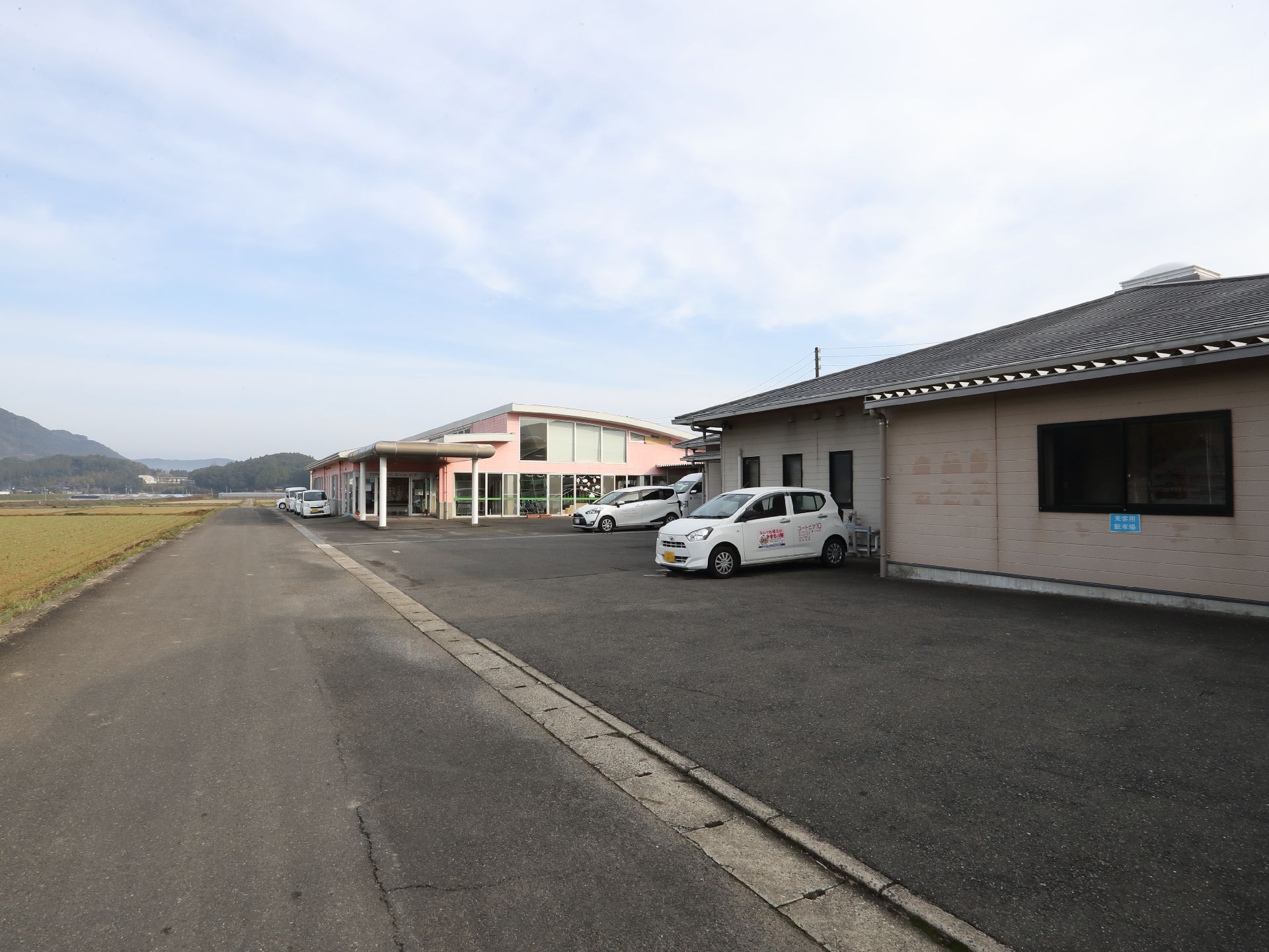 大きな看板には系列の介護事業所の名前が書かれ、その奥にはブラウンの外壁の建物がある。