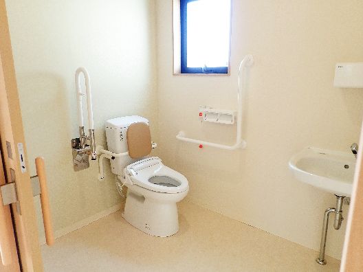 両サイドに手すりが付いたトイレは広く、背もたれ付きの便座が付き、大きな窓がある。