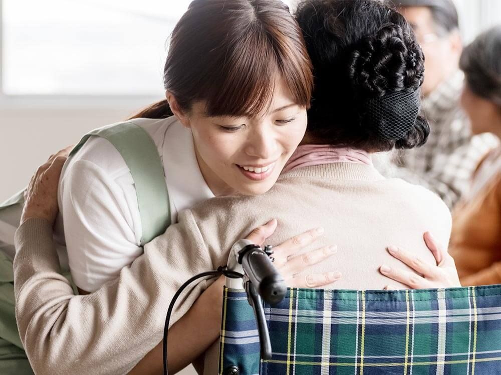 立ち入上がりろうとしている車いすの女性を補助するスタッフの表情。笑顔で対応している様子