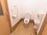 清掃の行き届いたトイレには、白い洋式便器と手洗い場が設置されている。左の壁には手すりと引き戸の扉が設置されている。