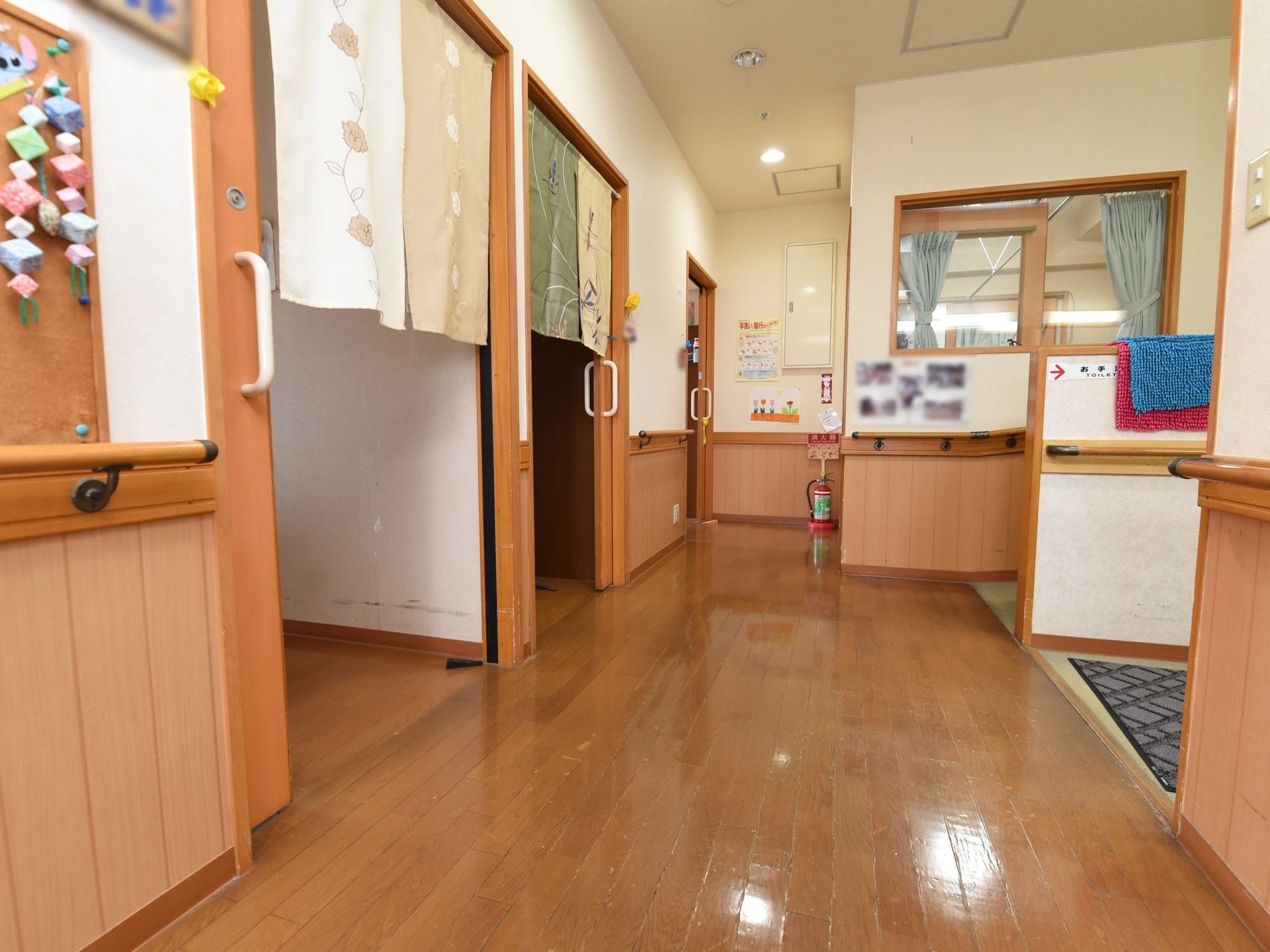 壁側に引き戸が並び、和柄ののれんがかけられている。床に消火器が置いてある。壁にはスナップ写真が飾られている。