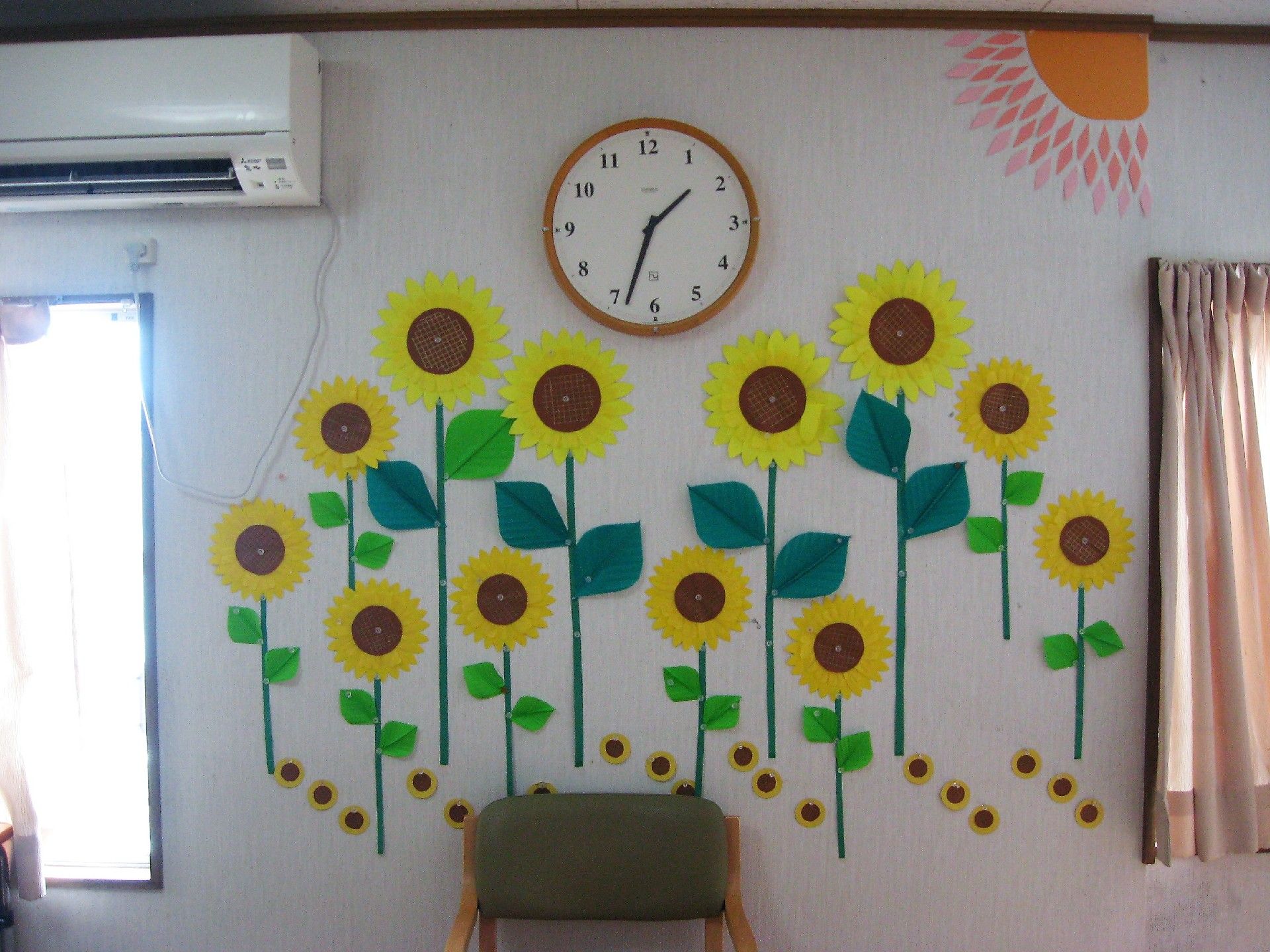壁には時計とエアコン、そして色画用紙で作られたひまわり畑がある。
