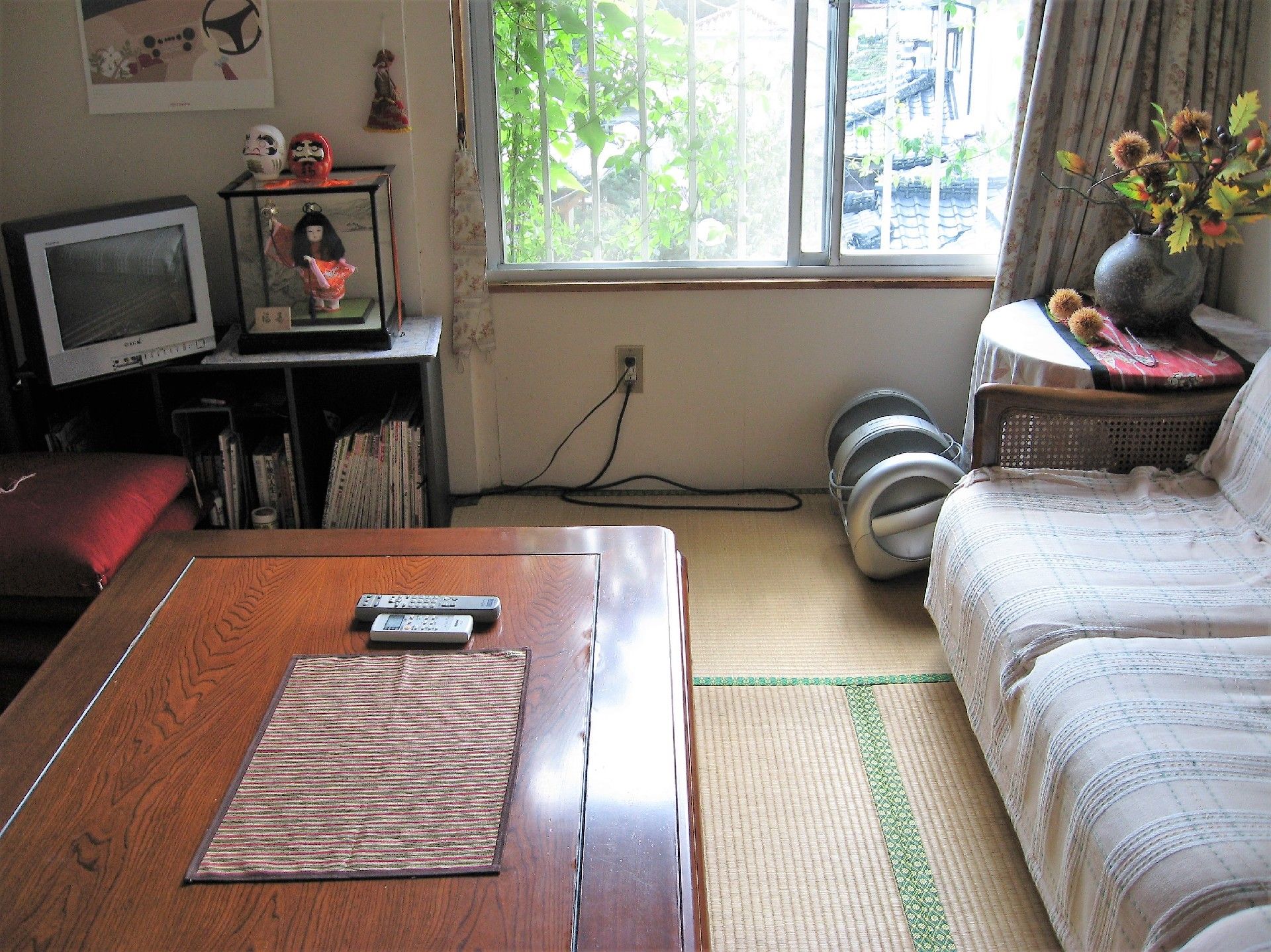日本人形やテレビ、ソファが置かれた畳の部屋。日当たりがよく家庭的な雰囲気。