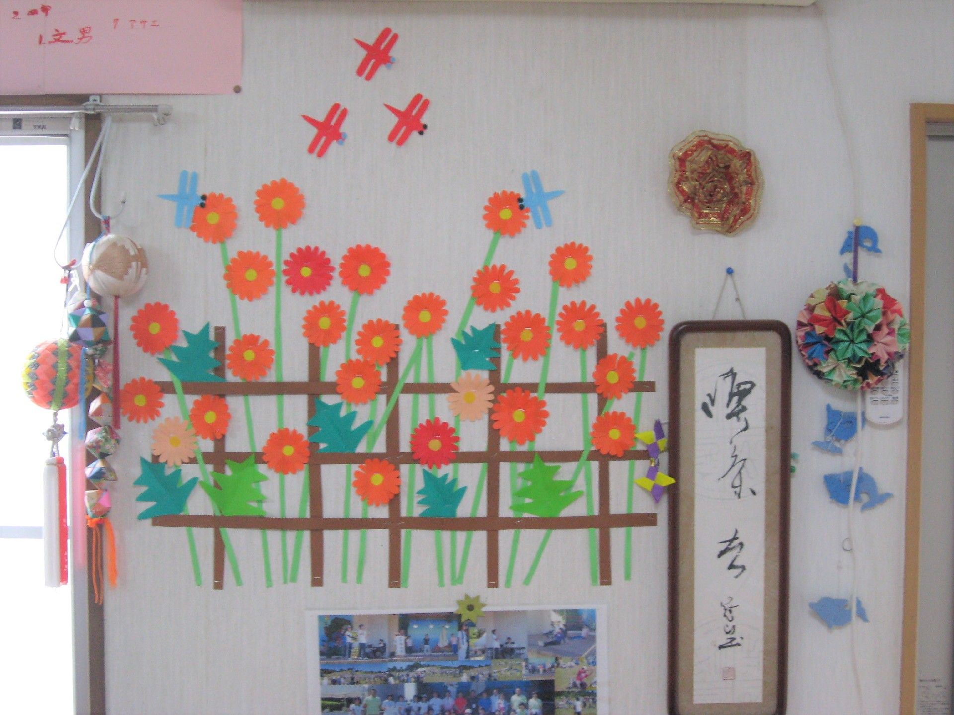 色画用紙で作られた手作りの飾りが壁に飾られている。トンボと秋桜。