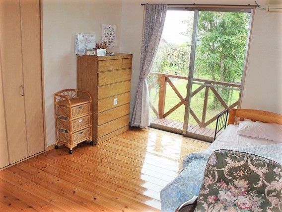 フローリングの部屋。木のタンスやベッドが置かれ、外の景色も見える。