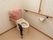 便座周囲にスペースを設けた多目的トイレで、手すりと洗浄水タンクに布がかぶせてある。手すりは木製のものが便座両側に設置されている。