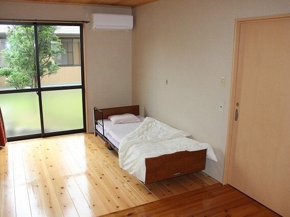 大きな窓から庭が見えるベッドとエアコンが設置されたフローリングの居室