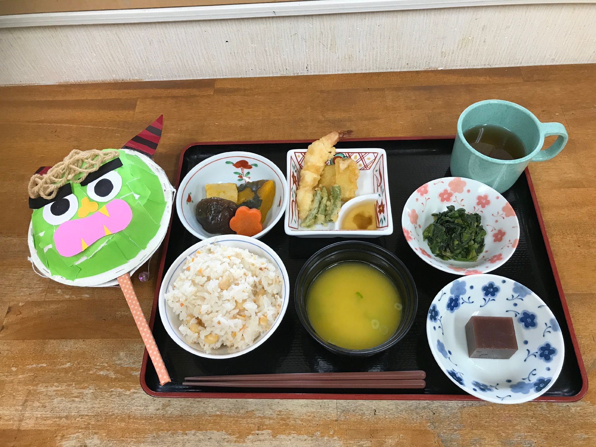 天ぷらや野菜の煮物、炊き込みご飯がセットになった食事と、鬼の顔のでんでん太鼓