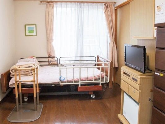 寝具付きのベッドやテレビが置かれたフローリングの居室には収納家具も付いている。