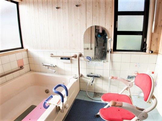 浴槽の周りにはたくさんの手すりが付き、木目調の壁には大きな窓も付いている。シャワーチェアとシャワーも完備。
