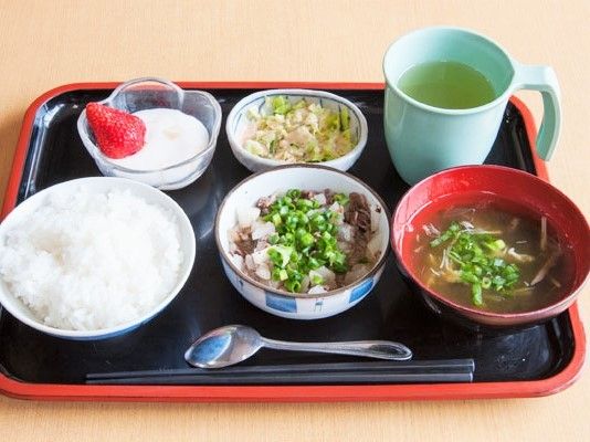 白いご飯にみそ汁、肉料理やあえ物、イチゴ付きのヨーグルトが並べられた黒いトレー。