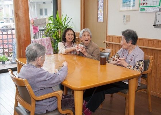 3名の女性入居者とスタッフが楽しそうに話をしている様子。入居者は座り、スタッフはテーブルのそばに膝立ち。