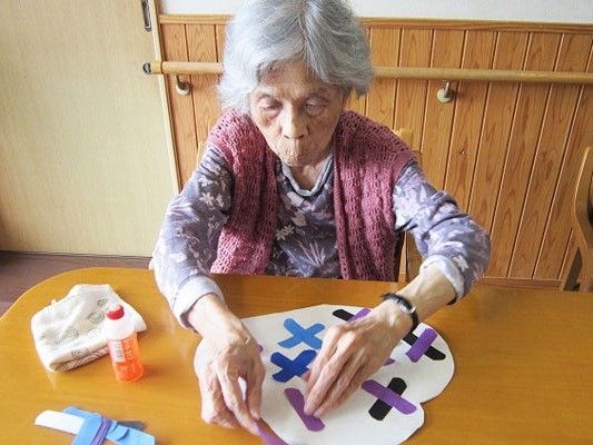 テーブルの上で熱心に工作に取り組んでいる入居者。ハサミやノリ、折り紙も置かれている。