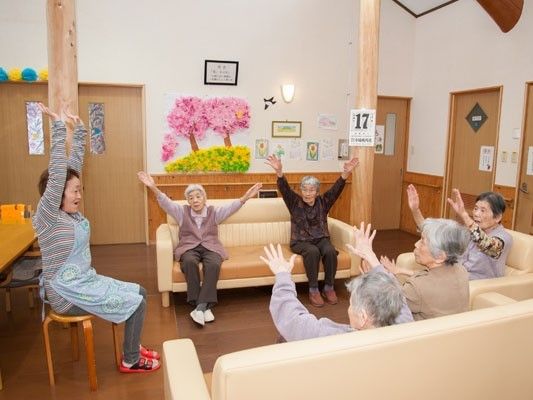 丸椅子を囲むようにソファが3つ置かれ、スタッフが指導しながら体操を行っている様子。