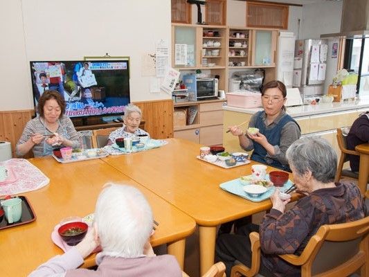 食卓は入居者とスタッフが一緒に囲み、テレビも付いている。奥にはキッチンがある。