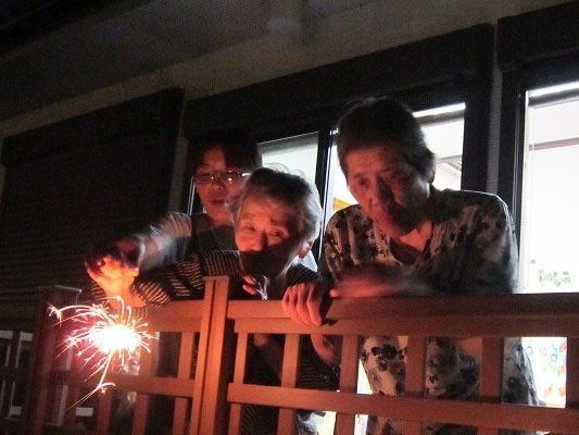 手持ち花火を持って楽しむ入居者とそのそばで見守るスタッフ。