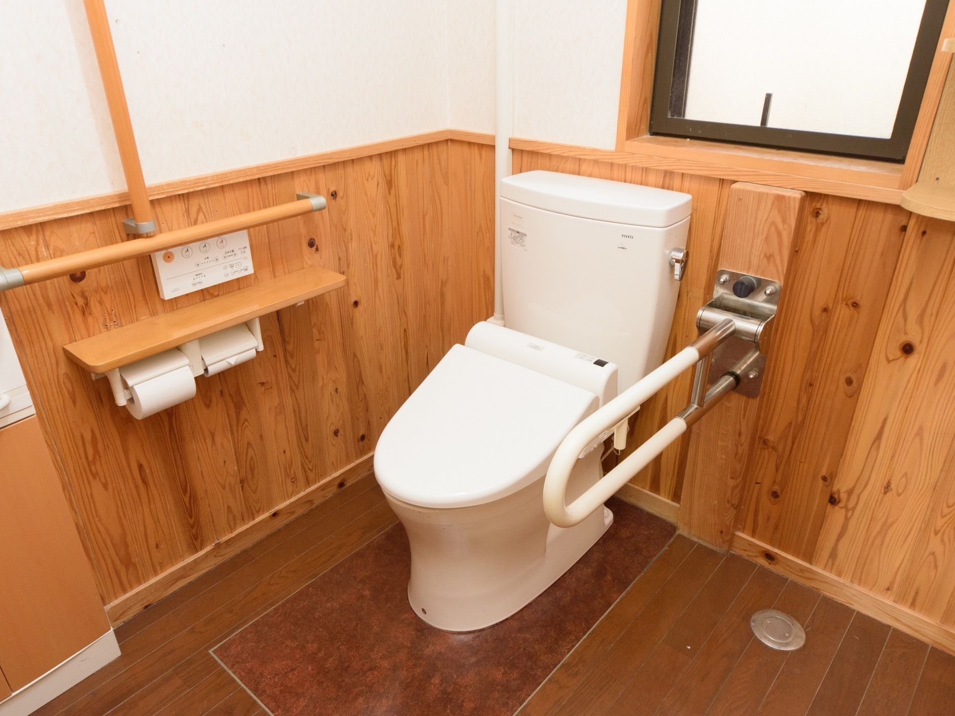 自然の木目を壁にあしらったトイレである。温水洗浄便座が完備されており、可動式手すりが設置されている。
