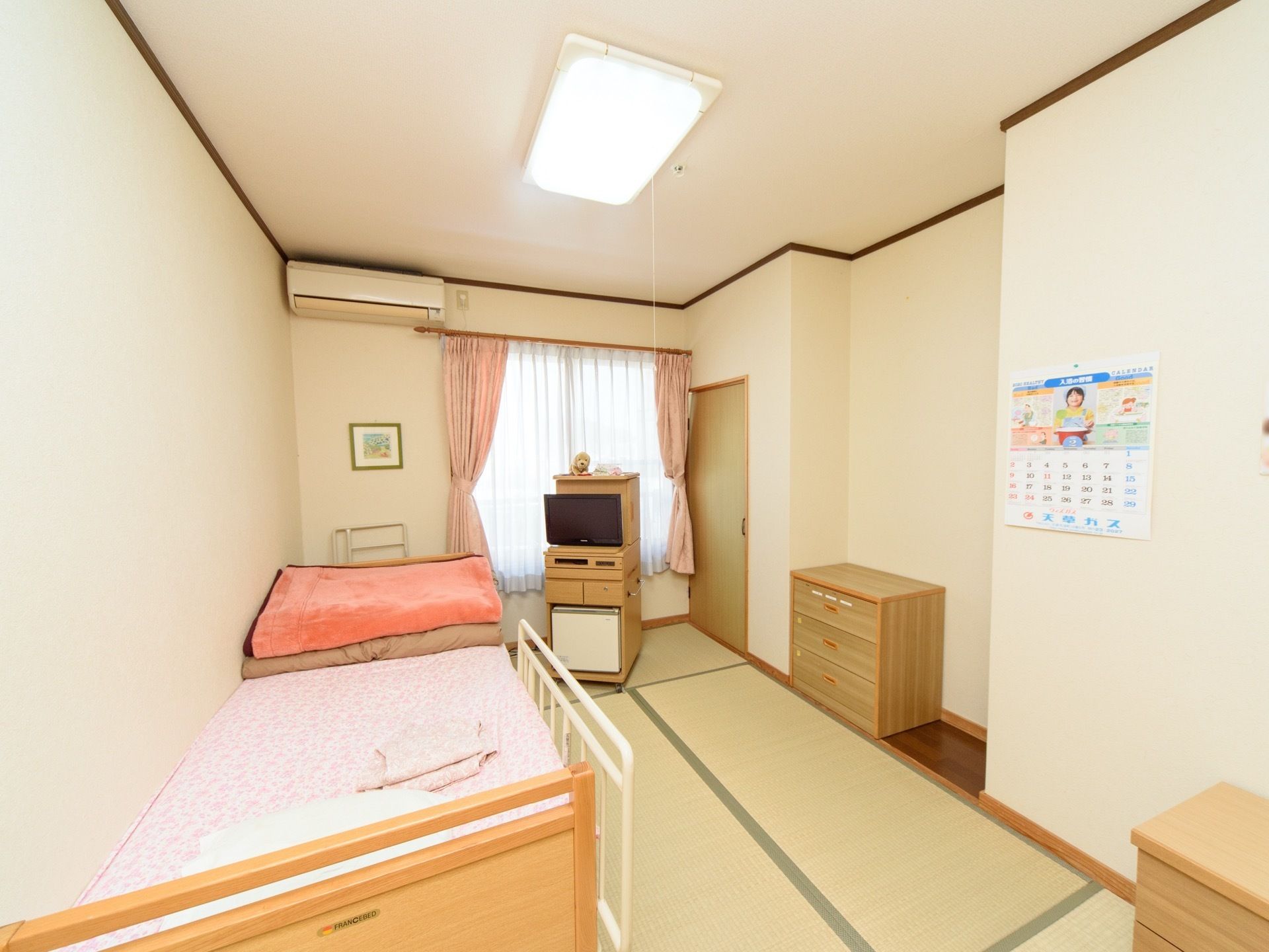 白い壁に畳敷きの居室である。造り付けの収納があり、窓やエアコンが設置され介護用ベッドが置かれている。