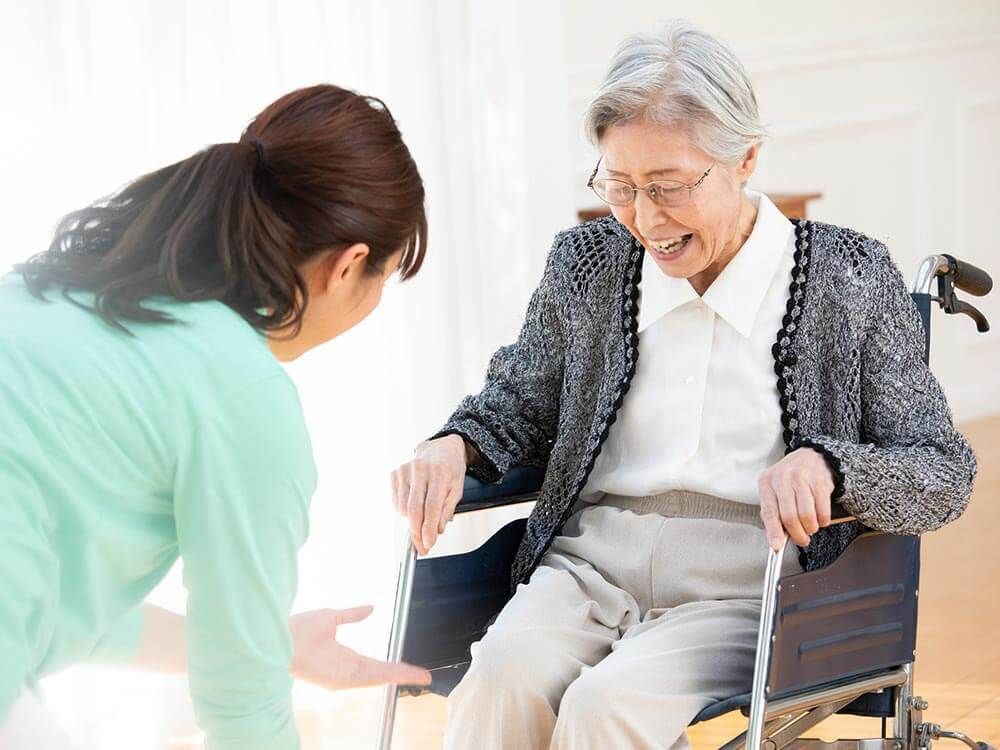 眼鏡をかけた車いすの高齢女性が目の前にいる髪の長い女性が差し出す手を嬉しそうに見ている。