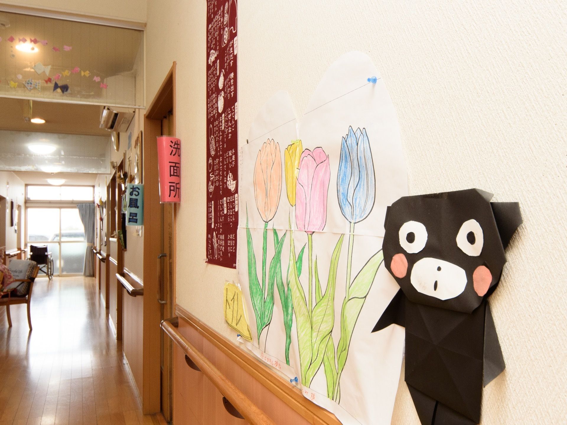 通路の壁に、折り紙でつくった作品と、絵が飾られている。お風呂と洗面所の場所がわかりやすいように案内表示がされている。