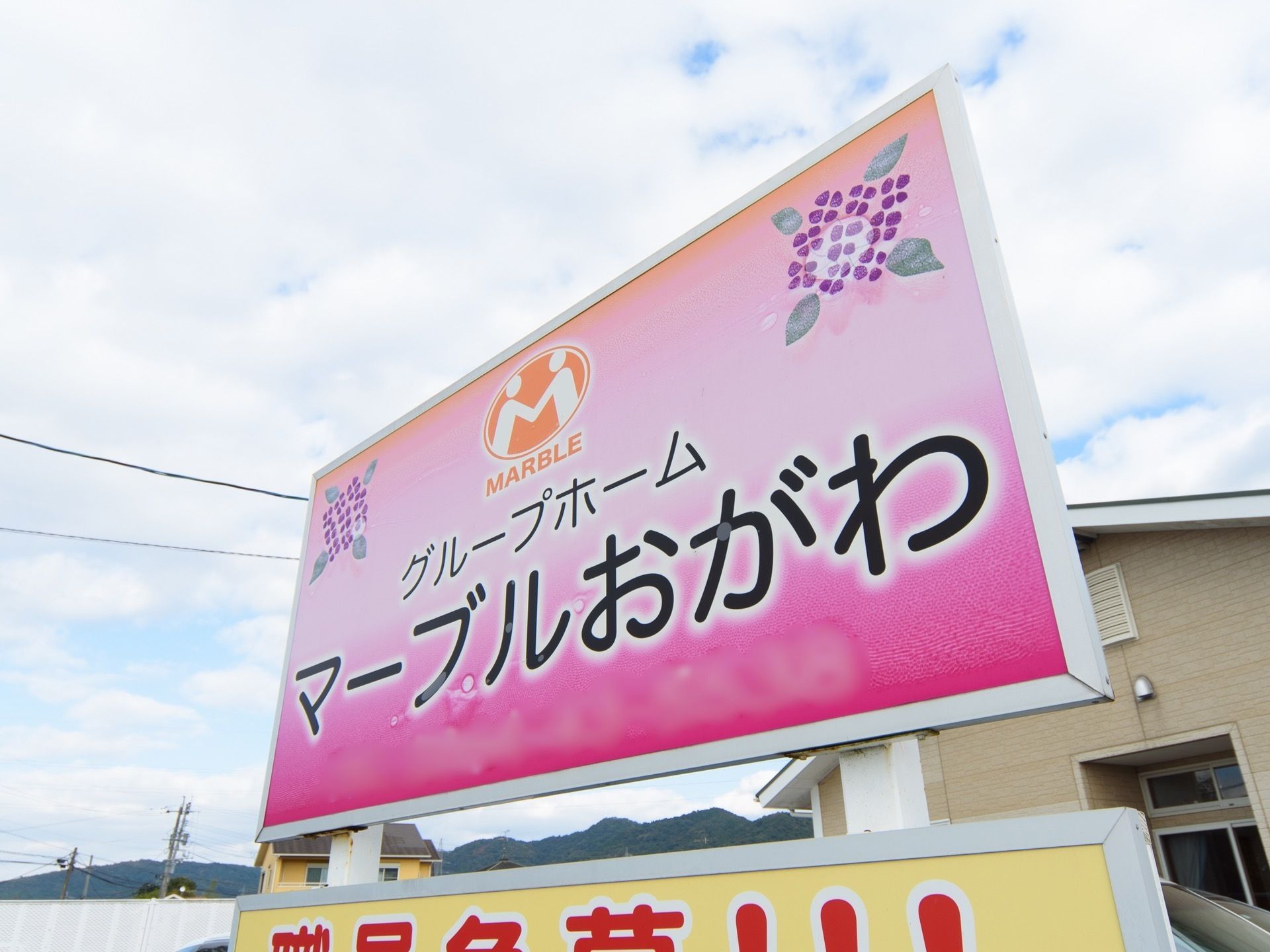 施設名が黒い文字で大きくかかれた、ピンクの看板が掲示されている。文字のほかに、施設のロゴマークやあじさいのイラストがある。