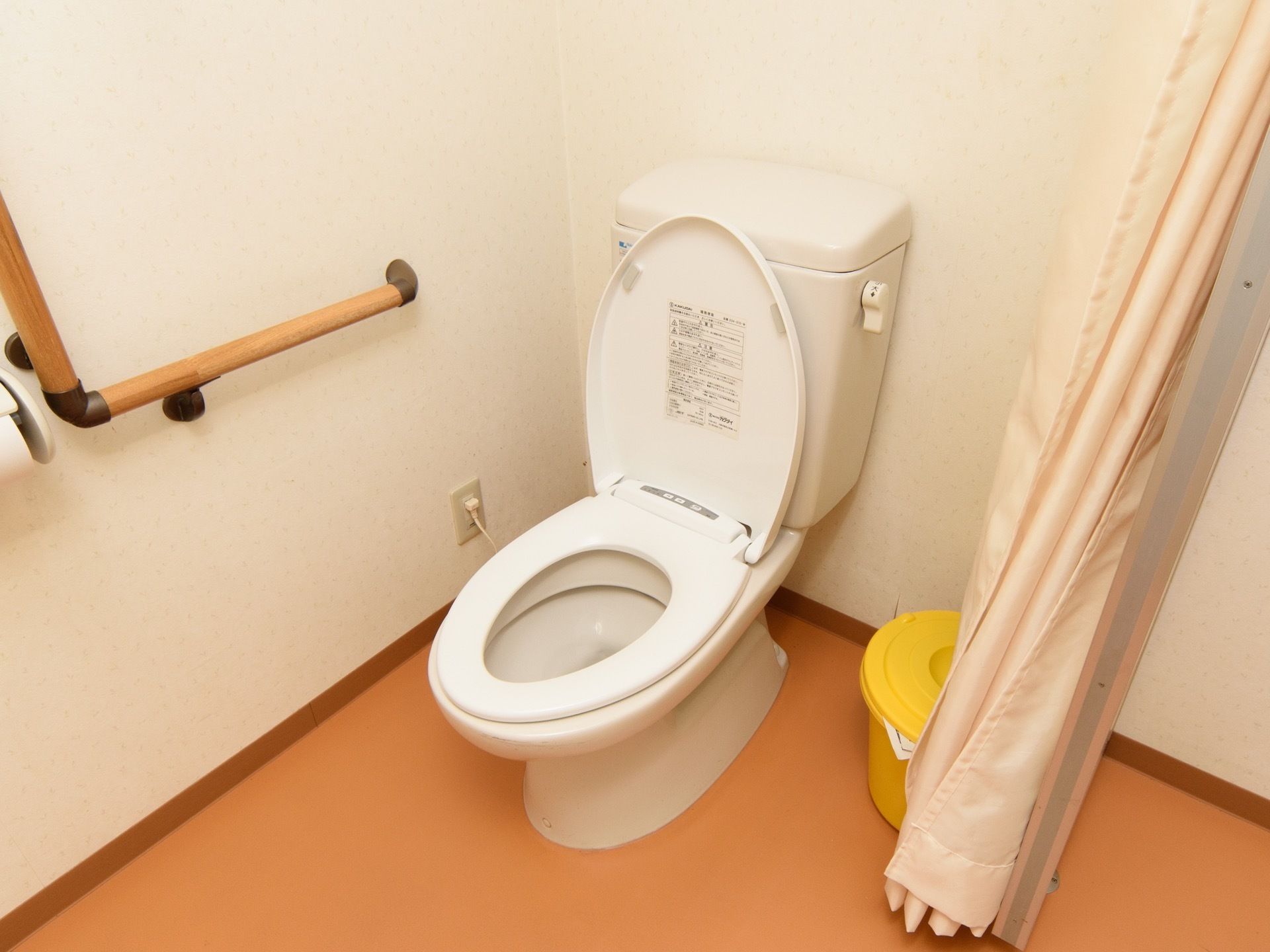 トイレは、シャワーカーテンで目隠しができるようになっている。壁には、Ｌ字型の手すりが設置されている。