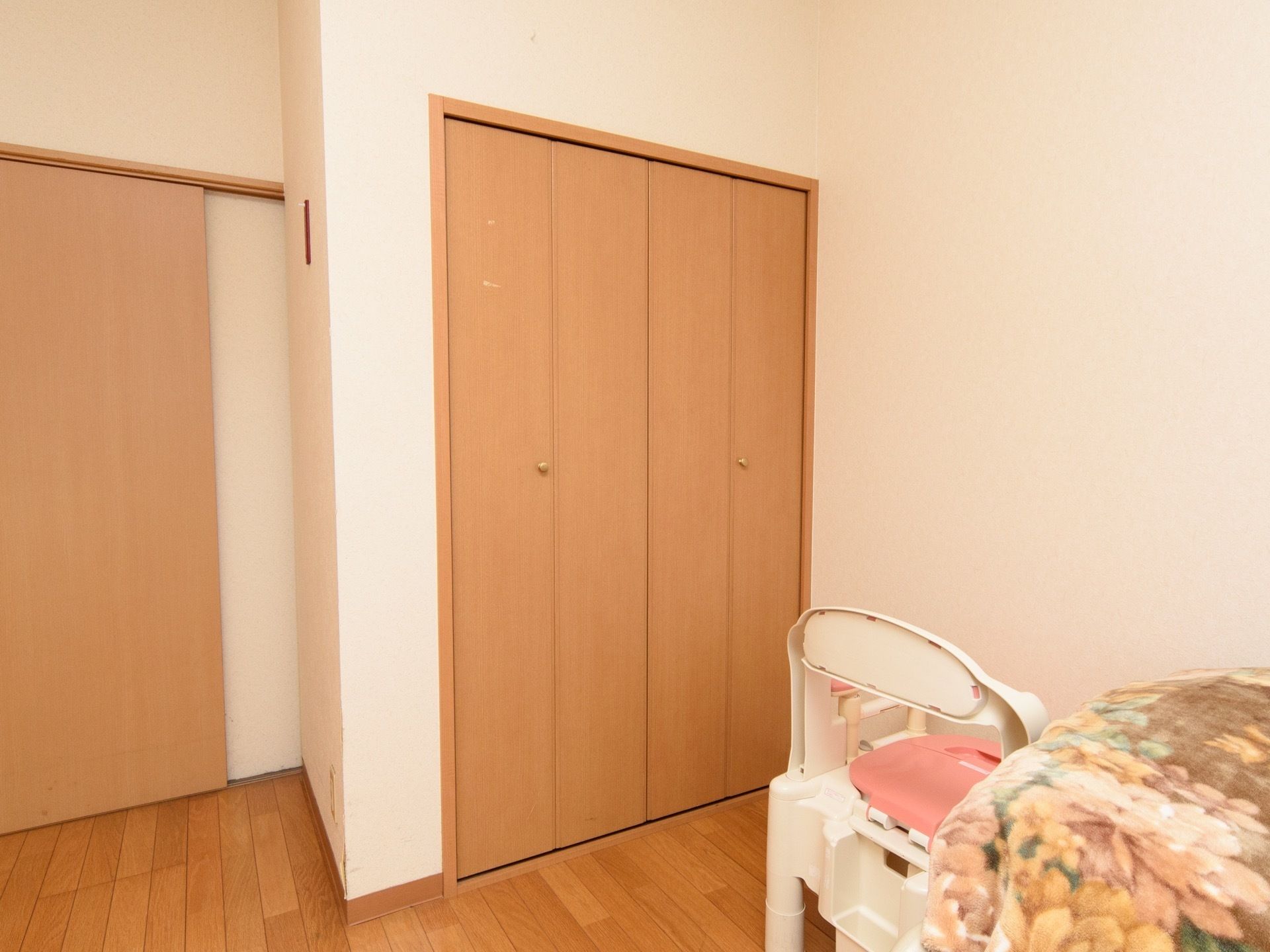 居室に設置された収納スペース。扉は木目調で、丸い取っ手がついている。収納スペースの前には、椅子や介護用ベッドが置かれている。
