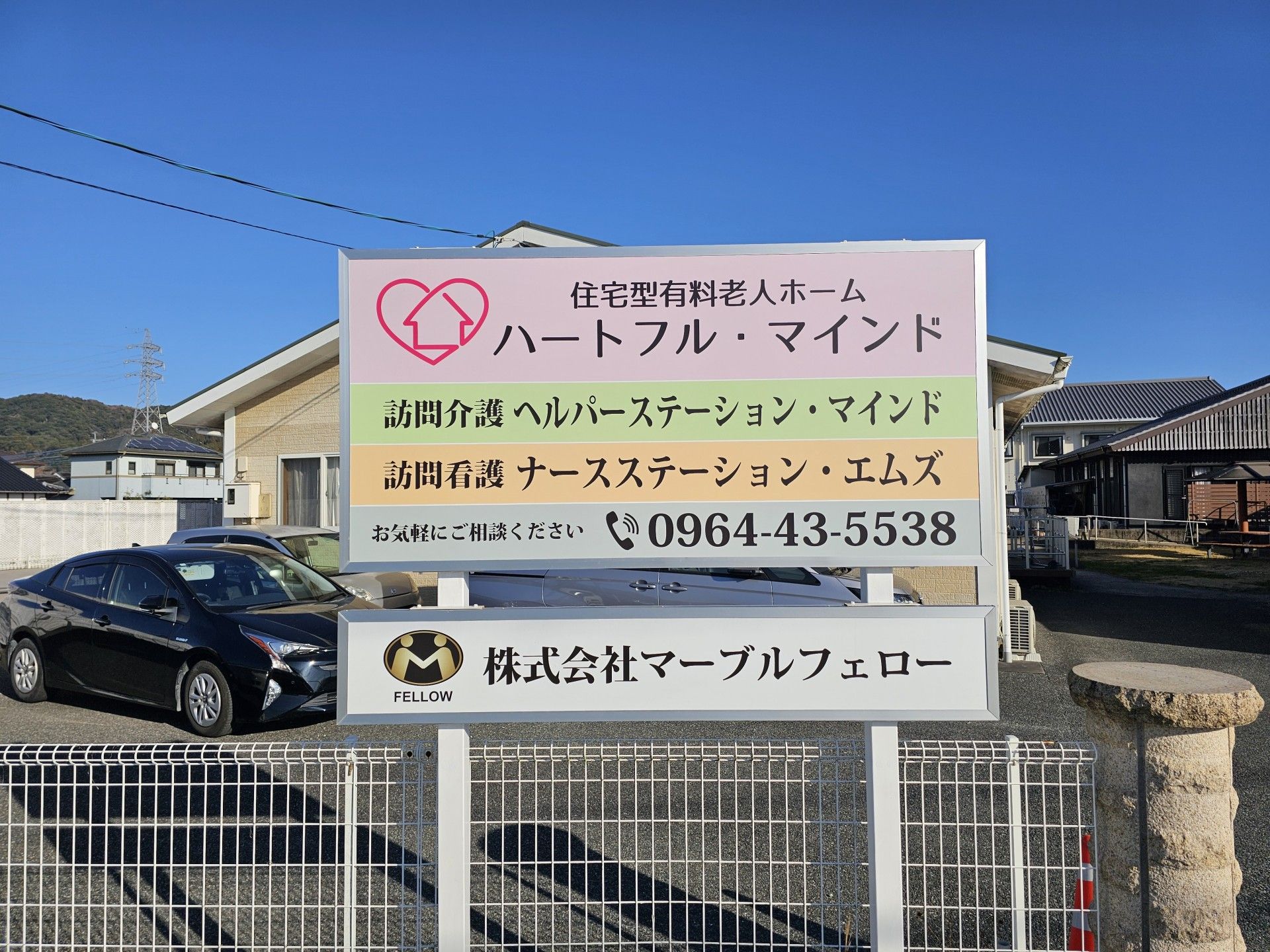 施設名が黒い文字で大きくかかれた、ピンクの看板が掲示されている。文字のほかに、施設のロゴマークやあじさいのイラストがある。