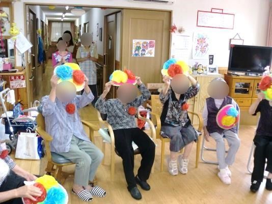 レクリエーションの様子。紙で出来た花を持った高齢者たちがさまざまなポーズをとっている。
