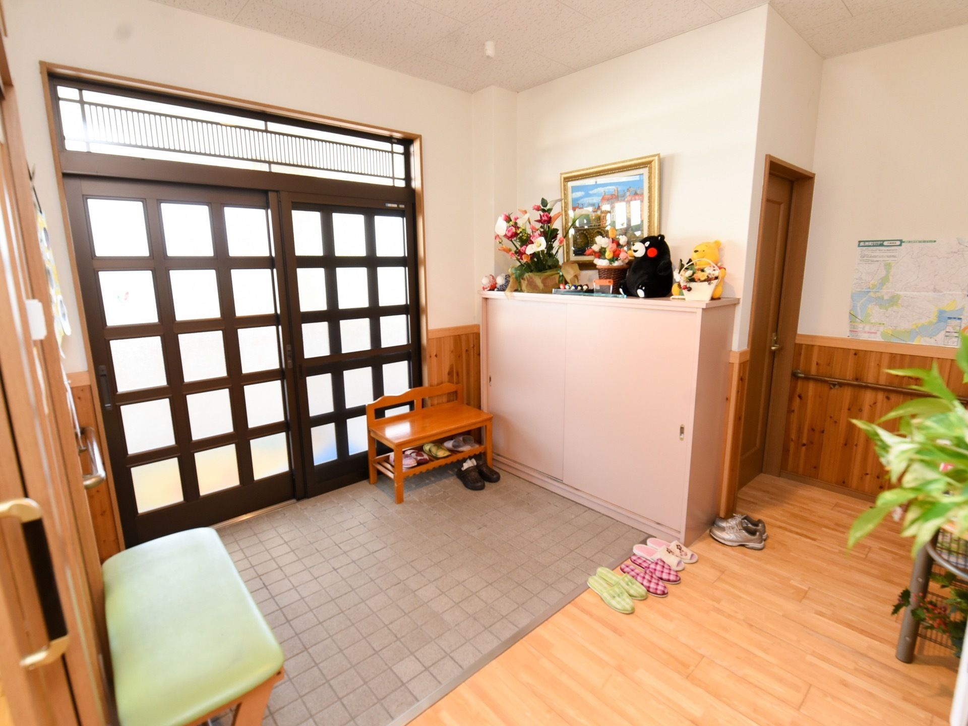 格子柄の引き戸の扉でできた入口である。壁際には大きな下駄箱があり、その上にぬいぐるみや花が飾られている。