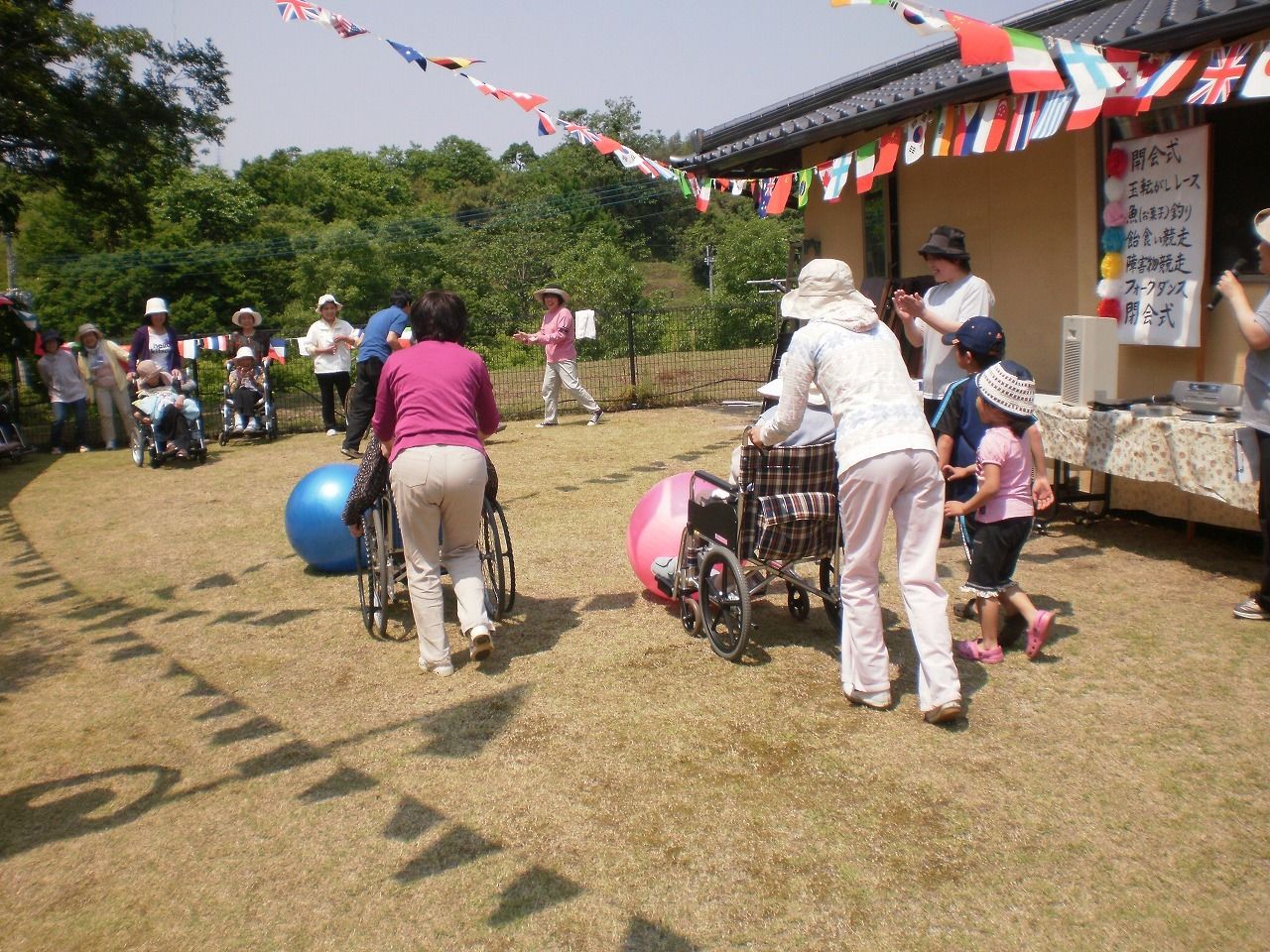 敷地内の庭で車いすの入居者がスタッフに押してもらいながら大きなボールを押している様子。