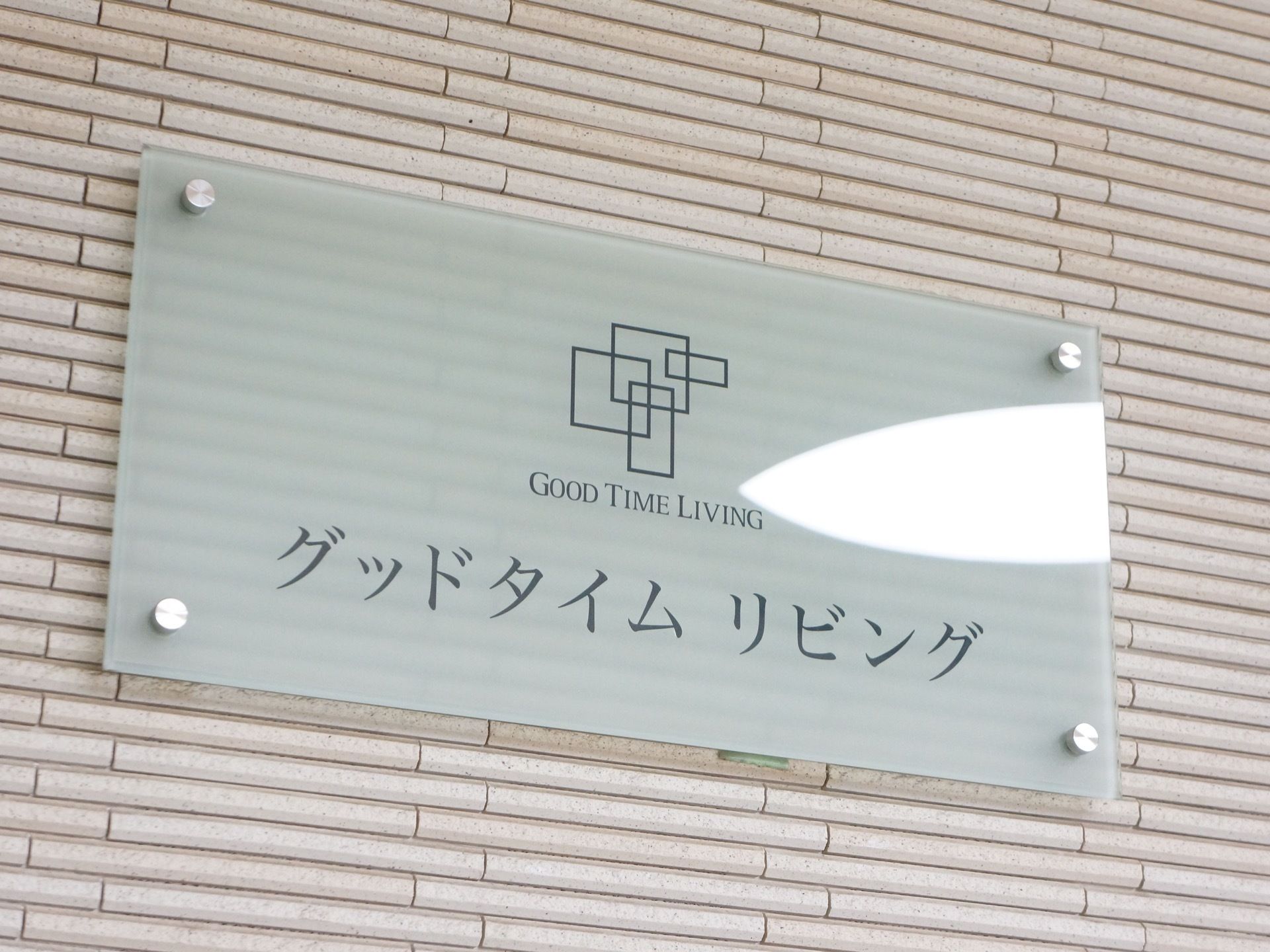 施設名称とロゴマークがアクリル板に記載され、壁にビス止めされている。スッキリとしたデザインで分かりやすい。