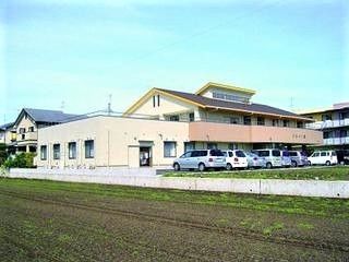 三角屋根が付いた建物は駐車場付きで、周辺には田畑が広がっている。