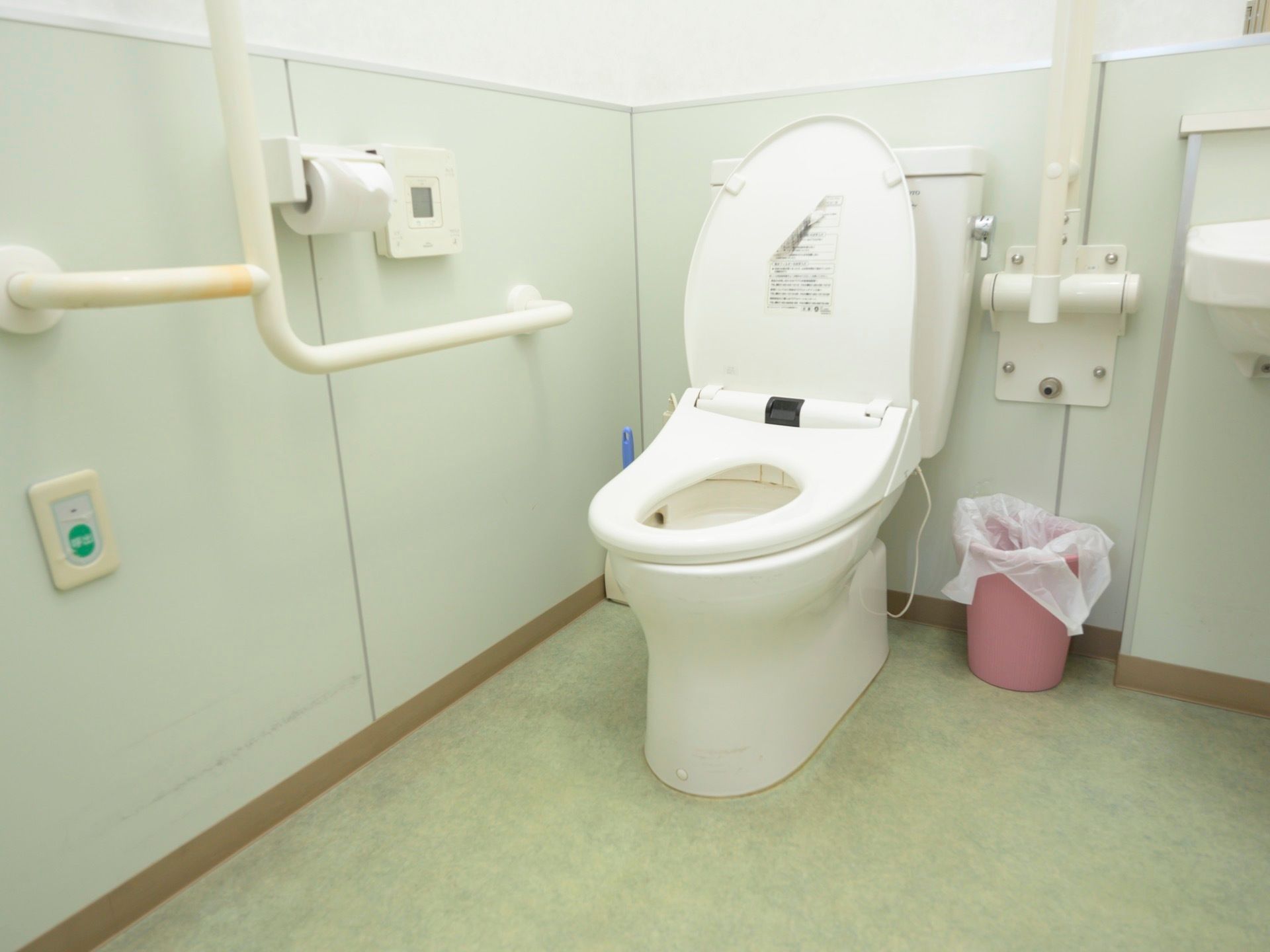 ナースコールが完備されているトイレで、温水洗浄機能付きの便座が採用されている。床には、ごみ箱や掃除用具がある。