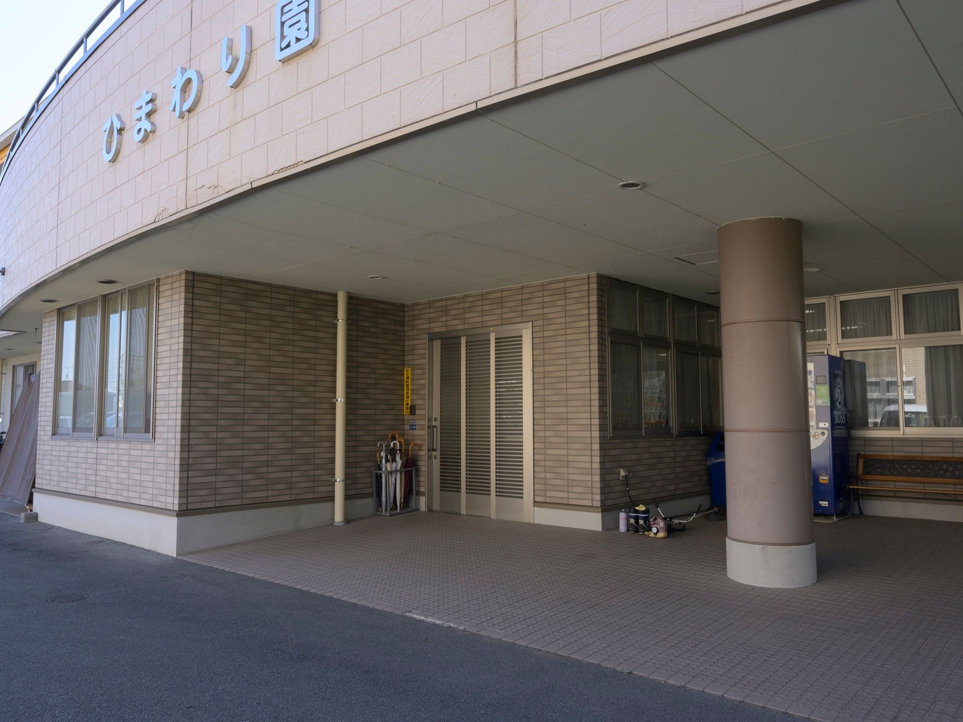 玄関横に、木製のベンチや自動販売機が設置されている。外壁はブラウンを基調としたタイル張りとなっている。