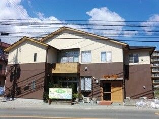 三角屋根が付いた２階建ての建物はブラウンと白の外壁で、日当たりのいい場所に建っている。