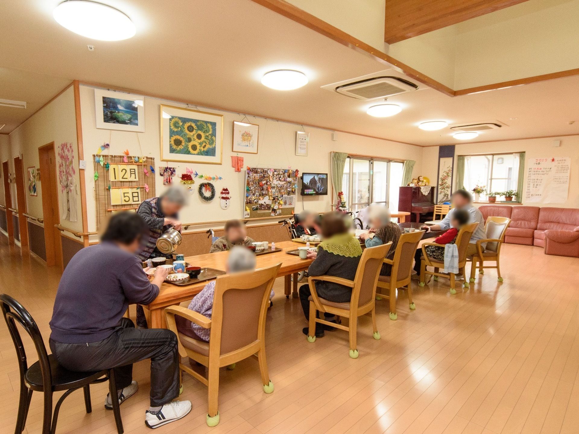 フローリングのダイニングにたくさんのテーブルセットが並んでいる。入居者様が腰を掛けて談笑などを楽しんでいる。