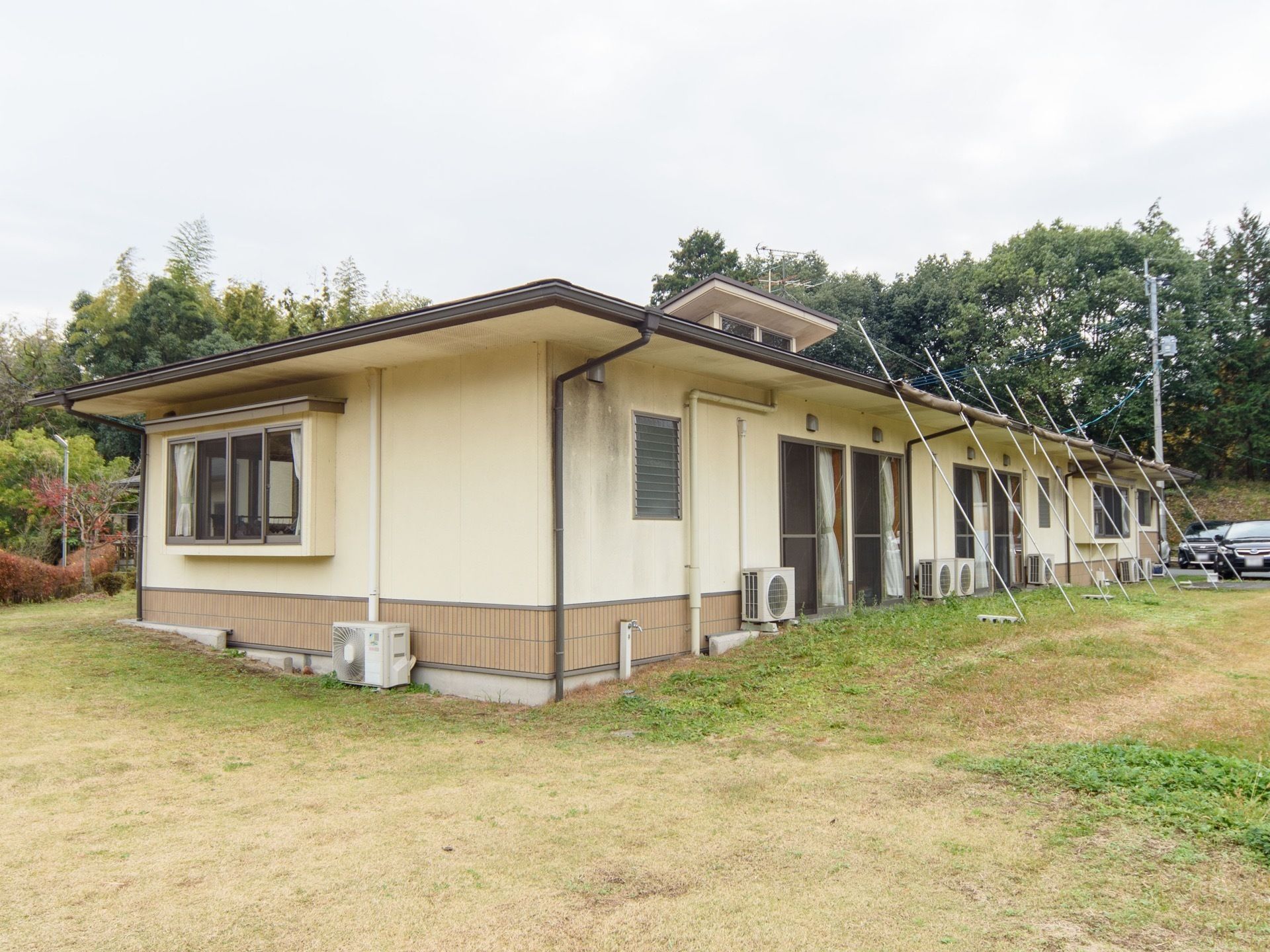 平屋建ての施設の周囲が、芝生で囲まれている。施設の横には駐車スペースがあり、車が何台かとめられている。
