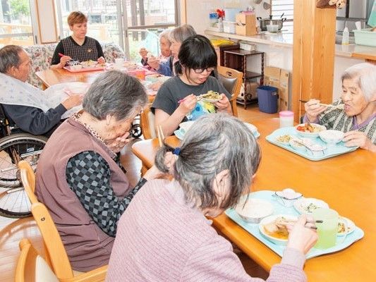 大きな窓が付いた明るい共有スペースで、スタッフと入居者が一緒にテーブルを囲んでいる様子。