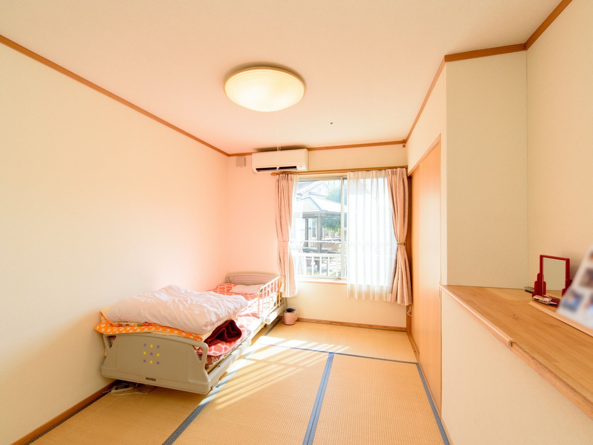 畳敷きの居室には電動ベッドが置かれている。腰高窓の上にエアコンが仕付けられており、小物などを置ける収納スペースも用意されている。