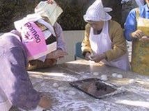 エプロンと三角巾を身につけた女性入居者が餅を丸めている様子。