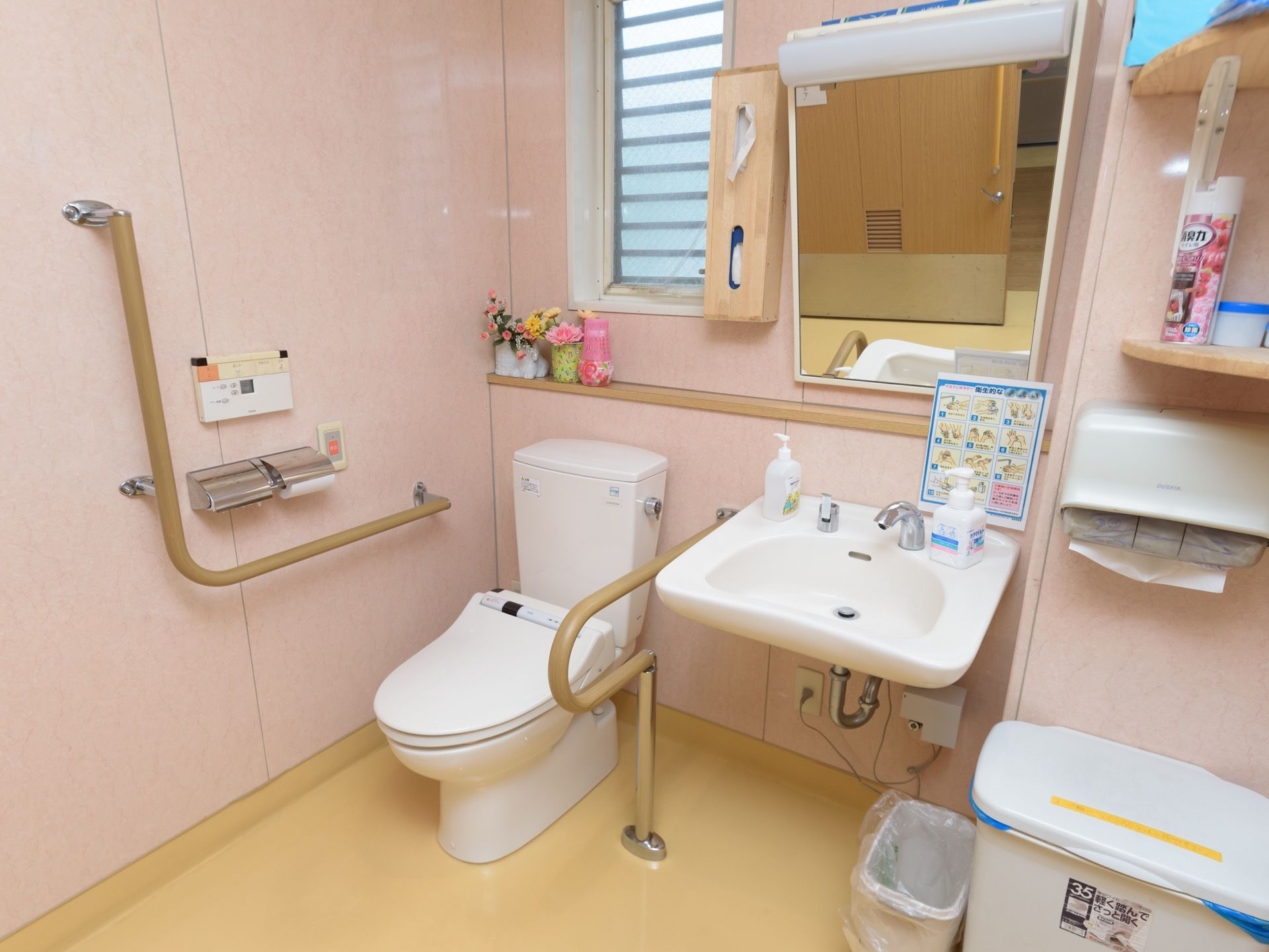 トイレには、洗面台や手すりが完備されている。ペーパータオルホルダーや鏡、収納棚が壁に設置されており、ゴミ箱が置かれている。