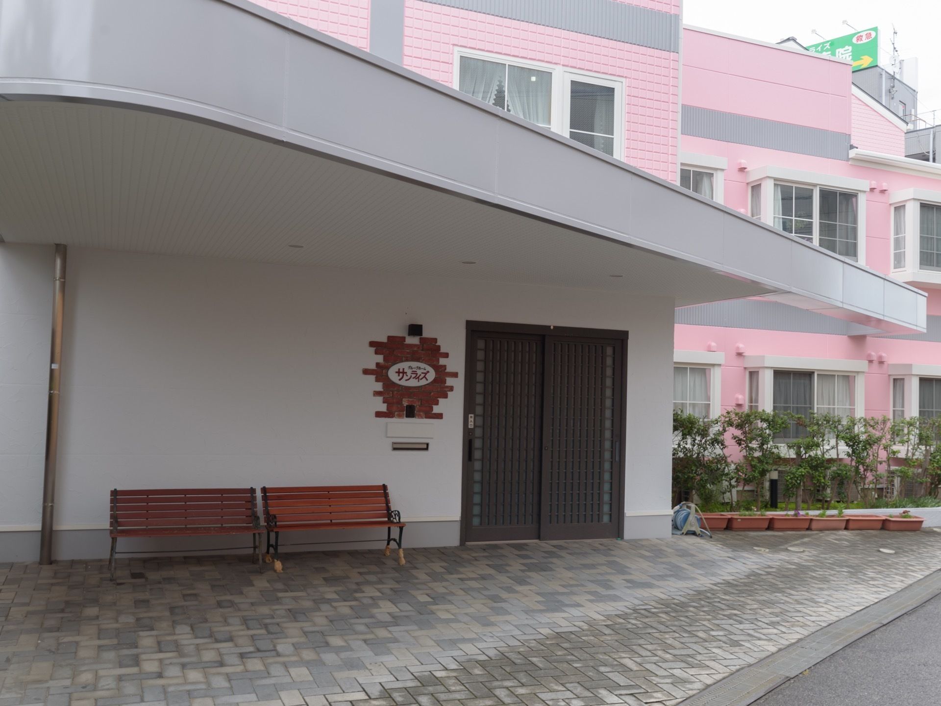 大きなひさし付きの広々としたエントランスである。壁際には、２台のベンチが設置されている。玄関扉は引き戸である。