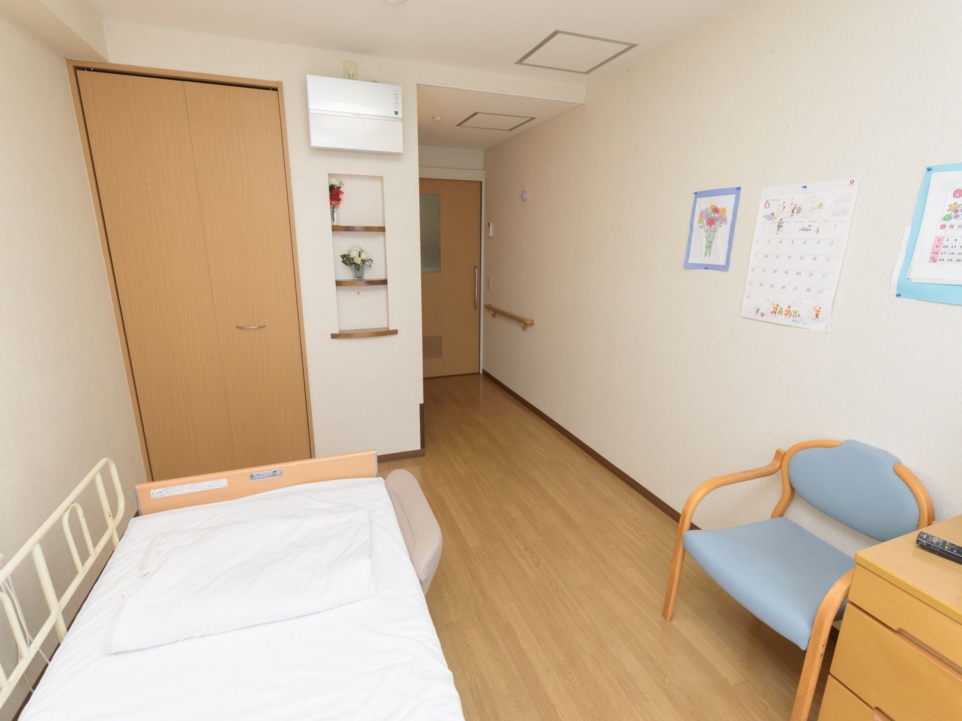 ワンルームタイプの居室である。クローゼットや介護ベッド、手すりが完備されている。壁際に椅子やチェストが置かれている。