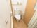 居室には、壁に手すりが設置されたトイレが完備されている。備品を置く棚が設けられており、カーテンが扉として採用されている。