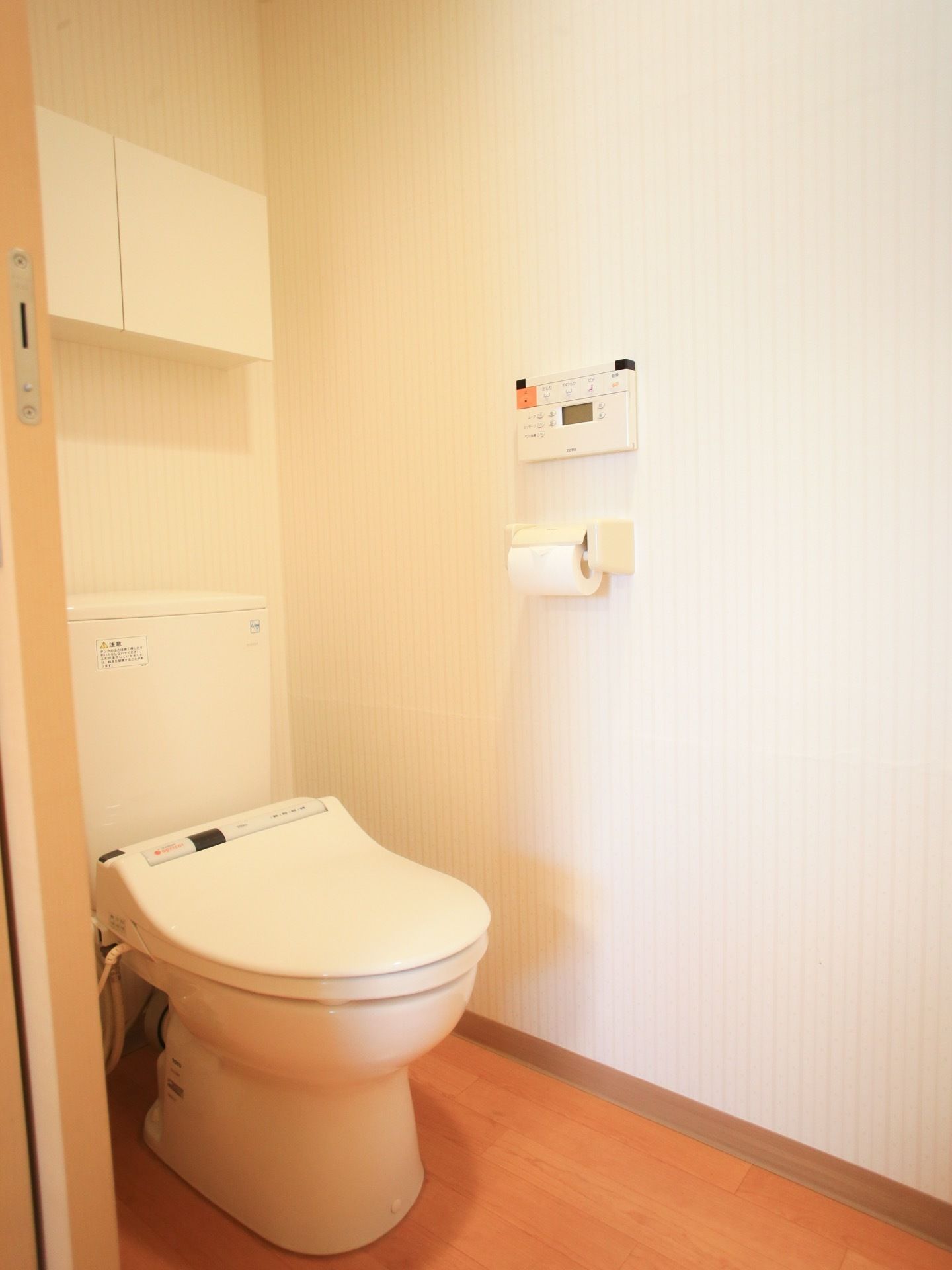 自宅のような落ち着いたトイレが居室に備え付けられている。緊急用ボタンが壁に取り付けられている。背面には収納棚がある。