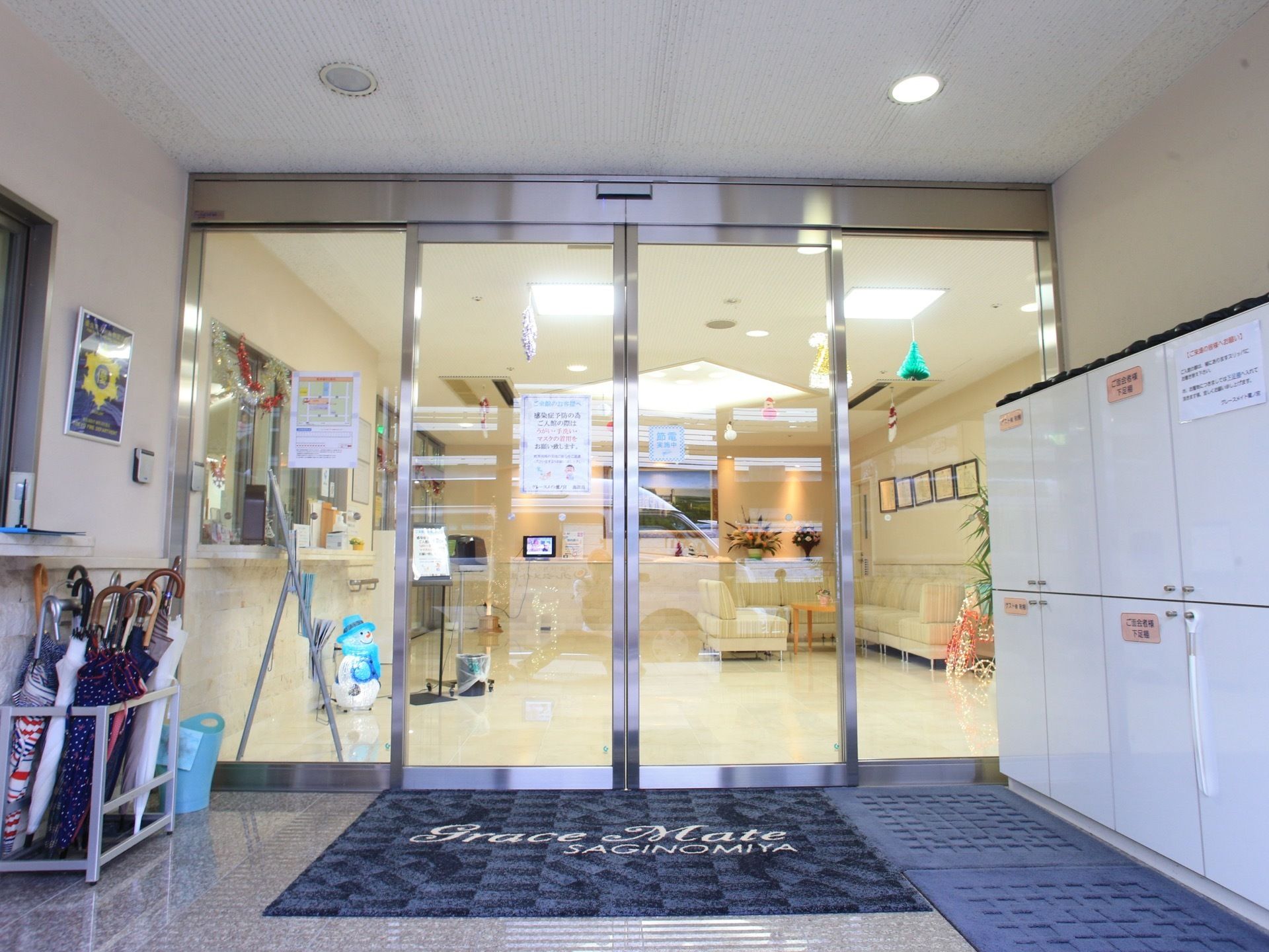 玄関はガラス張りの大きな自動ドアを採用している。フラットな床で安全に出入りできる。下駄箱も設置され、整頓された入口空間となっている。