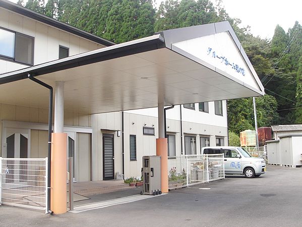 大きな車寄せが玄関部分に設置された白を基調とした2階建ての建物。周辺には緑が多い。