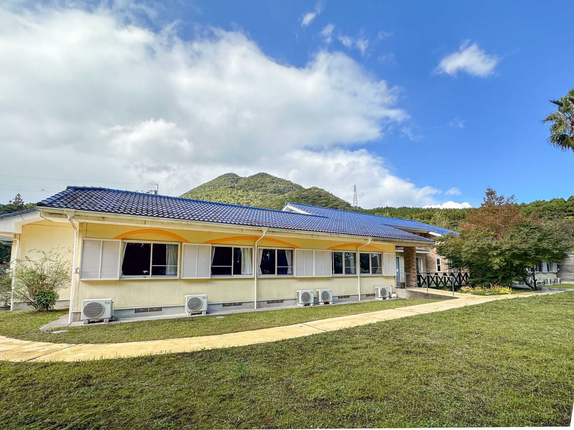 ブルーの瓦屋根とレンガ調の外壁が家庭的な雰囲気の建物。ウッドデッキが付いている。
