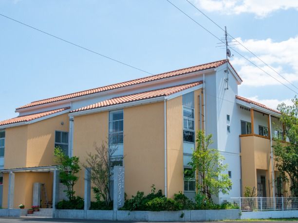２階建ての建物はオレンジ系の外壁でオレンジの屋根が付き、周辺にはたくさんの木が植えられている。